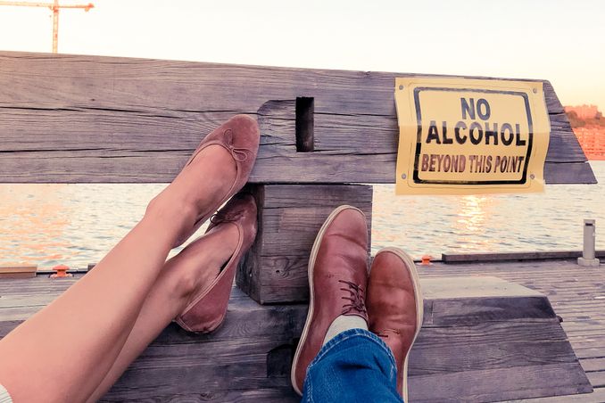PHP: A couples' legs rest on a fence with a sign that says 'No Alcohol Beyond this Point' to indicate success of Partial Hospitalization Programs 