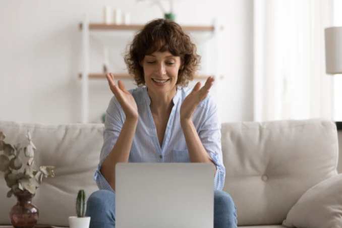 Choosing the right addiction rehab concept shown by woman clapping in relief above her laptop