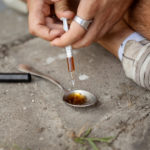 Heroin Drug Paraphernalia | Find Addiction Rehabs | Woman using syringe to withdraw heroin from spoon