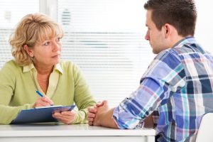 Codeine Addiction Recovery - A young man sits with his back to the camera while he talks to his therapist. She sits facing the camera looking at him taking notes on a clip board as he talks.