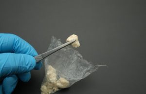 Crack Dependence - Close up image of a small baggie with several pieces of crack in it. A gloved hand holds a piece of crack with tweezers just above the bag.