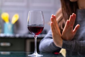 Alcoholism - A woman sits behind a glass of red wine with her hands up crossed as to say she is giving up alcohol.