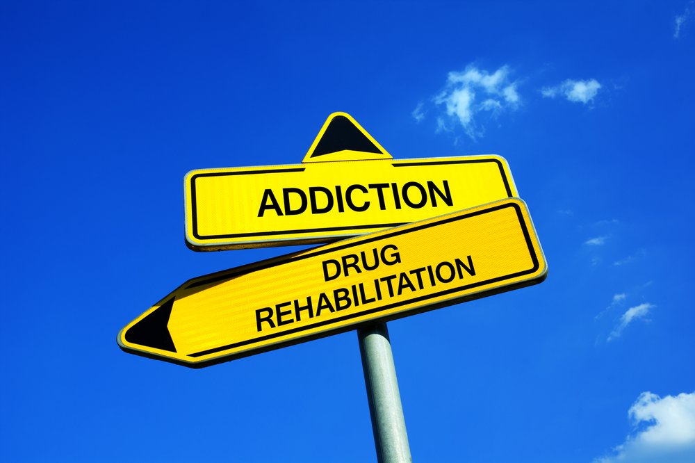 Celebrities In Recovery from Addiction - 2 fake road signs. The one on top says "Addiction" with an aarrow pointing up the bottom sign says "Drug Rehabilitation" with an arrow pointing to the left.