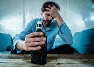 Do I Need Alcohol Rehab - Man sits alone on his couch drinking alcohol from the bottle. He should go to alcohol rehab to get better.