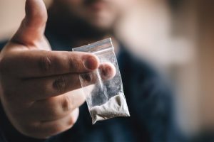 Drug Rehab - A man holds a small baggie of cocaine right in front of the camera.