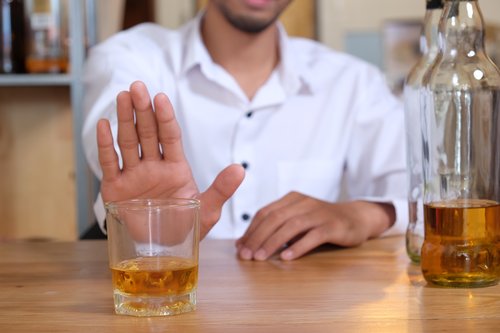 Stop Drinking Alcohol - A man sitting at a table in front of a bottle and glass of alcohol with the palm of his right hand up in front of the glass to say stop drinking alcohol or no I do not want a drink.