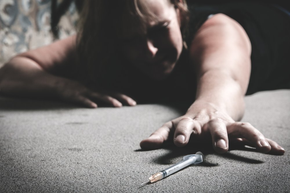 Hitting Rock Bottom - A woman lays on the ground and reaches out for a needle of heroine. She is struggling with addiction and is hitting rock bottom.