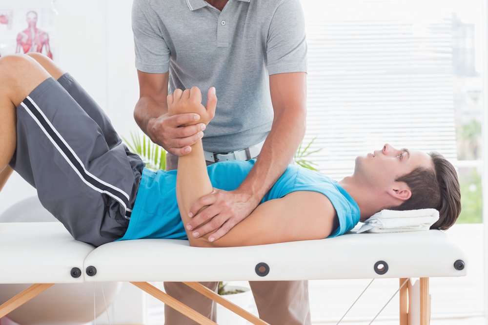 Addiction Recovery - A young man lays on a massage table as a masseuse works on his left hand and arm as he gets a therapeutic massage to enhance his holistic addiction recovery. To show concept of theta healing