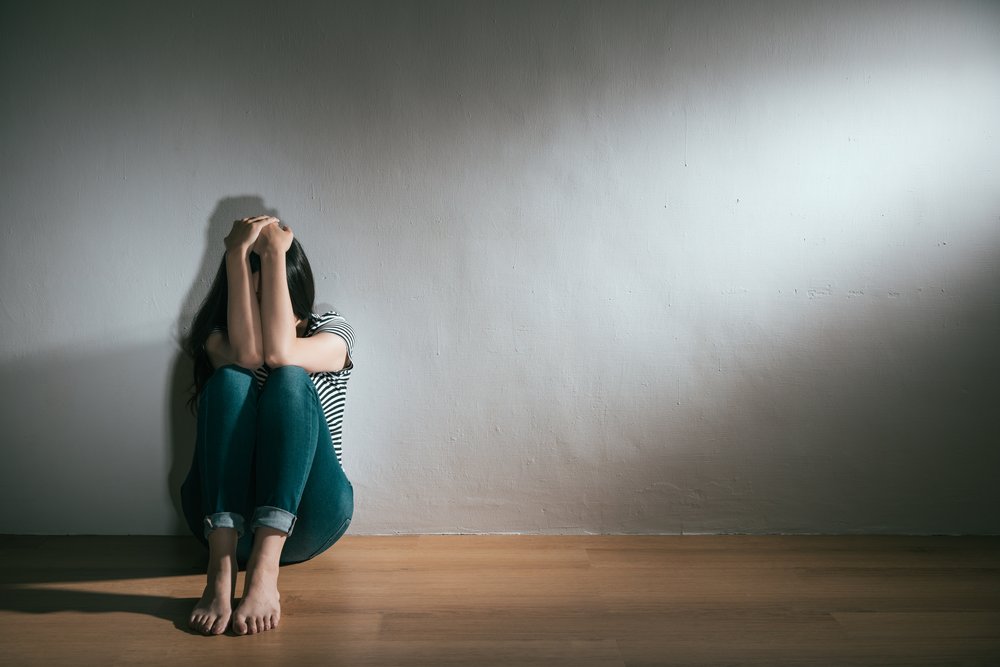 Depression - A woman sits on the floor with her hands on her head. She is dealing with a dual diagnosis of depression and alcoholism.