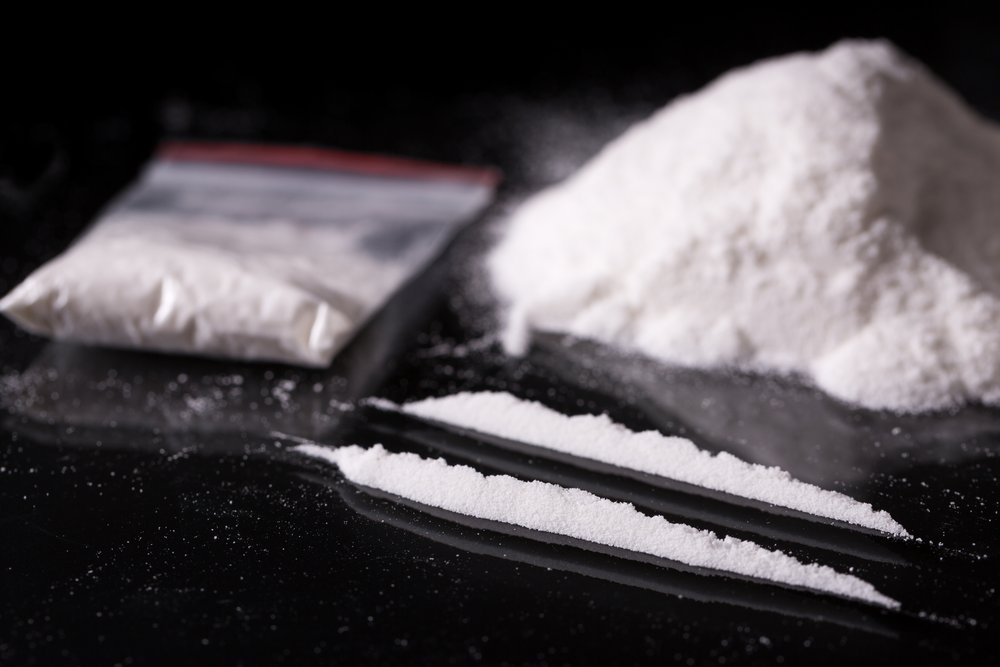Drug Addiction - Close up photo of a small pile of cocaine with a small bag next to it and 2 lines of cocaine in front of both.