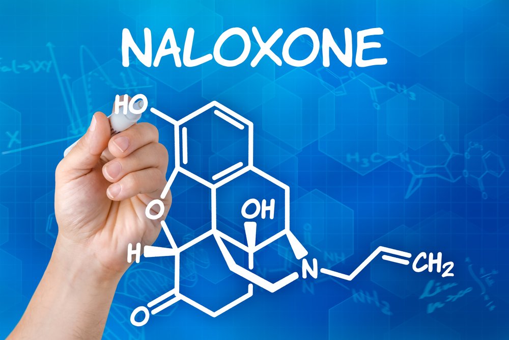 Narcan - Image of a hand writing out the chemical composition of Naloxone in white letters over a blue background.