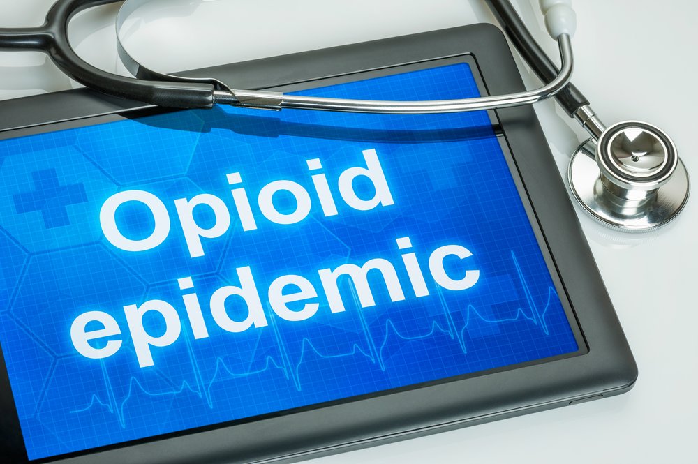 Opioid Epidemic - Close up of a tablet with a stethoscope around it with white block letters that say "Opioid epidemic".