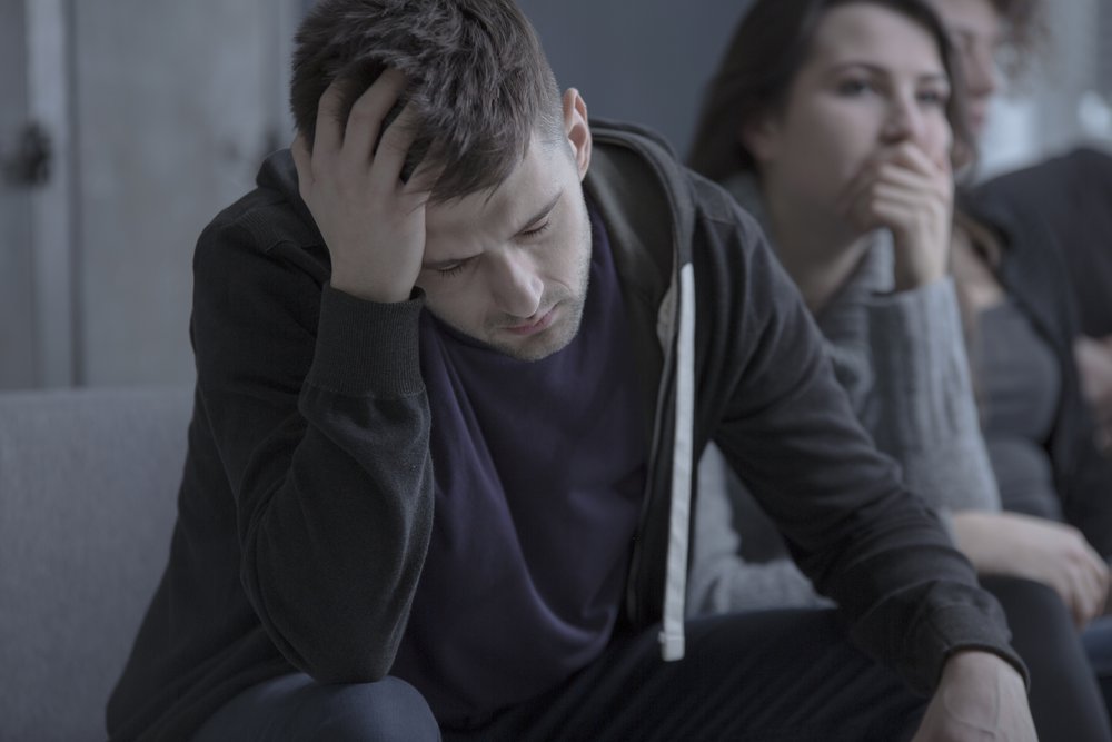 Withdrawal - A young man in addiction Treatment sit with his head down in group therapy with his hand is on his head and wonders why he still does not feel right. He is dealing with mood swings, irritability and fatigue. He is going through Post Acute Withdrawal Syndrome.