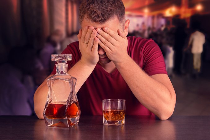 Man holds his head in his hands, with whiskey bottle in foreground, asking himself is there alcohol detox near me?
