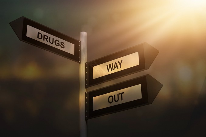 A signpost showing drugs in one direction and a way out in the opposite direction, to signify recovery from addiction