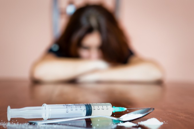 A woman with syringe in foreground illustrates the disease concept of addiction