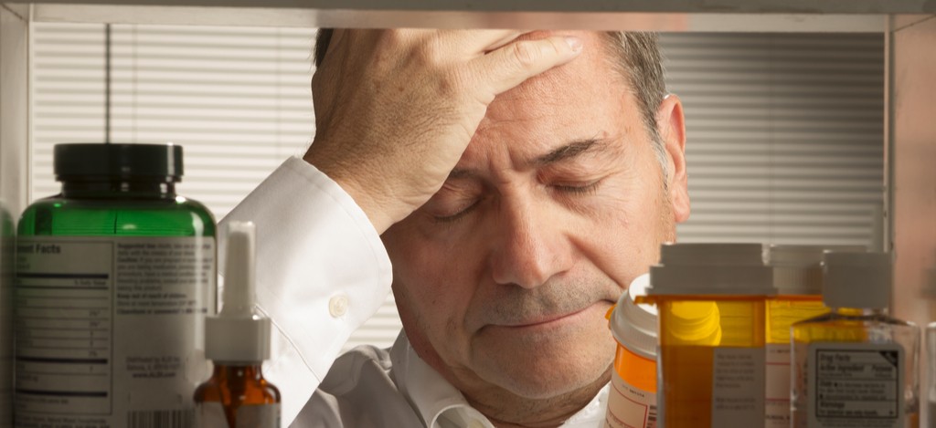 A man holds his head in front of his drug cabinet, wondering 'Is Klonopin addictive?