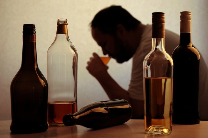 Is alcohol addictive? A man drinking alone, surrounded by bottles as a visual answer to the question