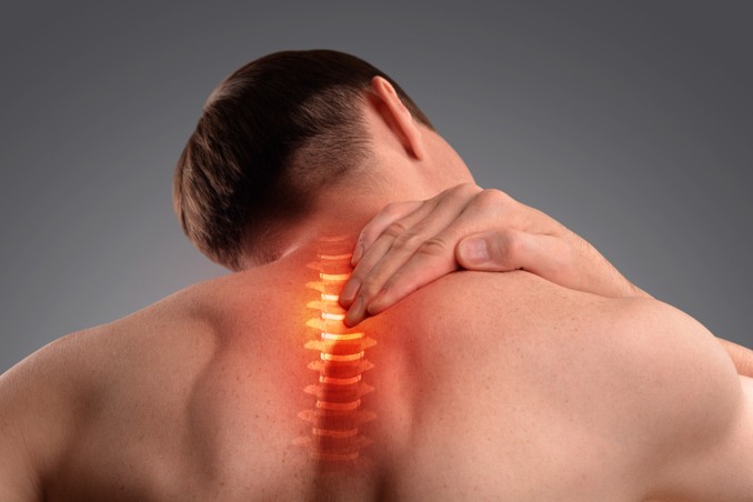 A man rubs his inflamed back and neck muscles, highlighted in orange 