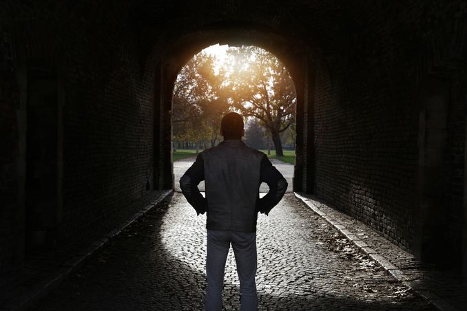 A man stands in darkened tunnel, looking into light and asking himself, 'is there alcohol detox near me?'