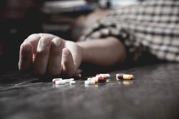Hand outstretched from unconscious man, with pills in foreground