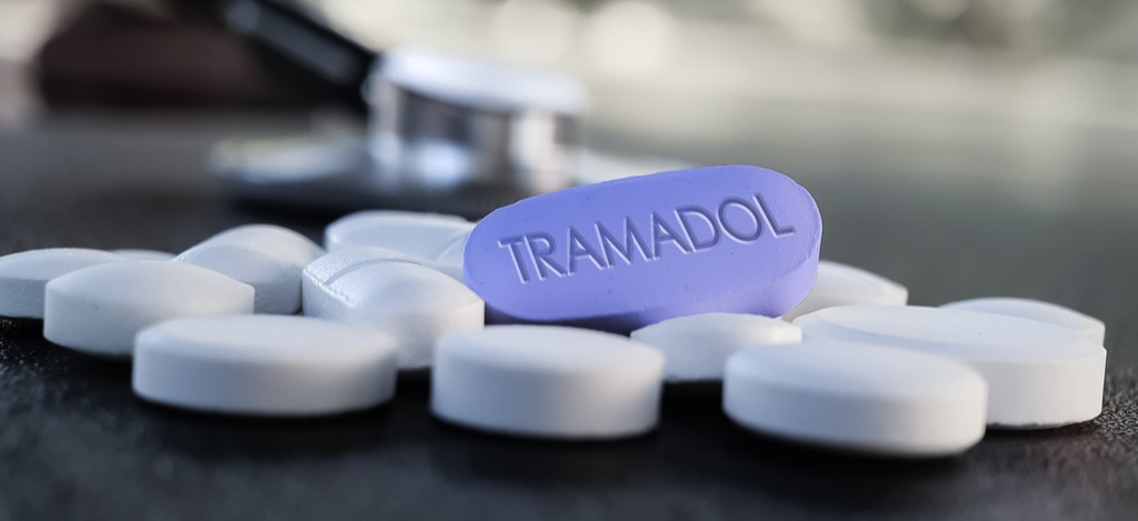 A purple Tramadol pill sits in contrast to other white pills on a desktop