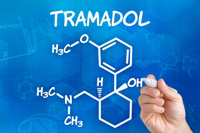 Chemical structure of Tramadol being written by a hand in white marker on blue background