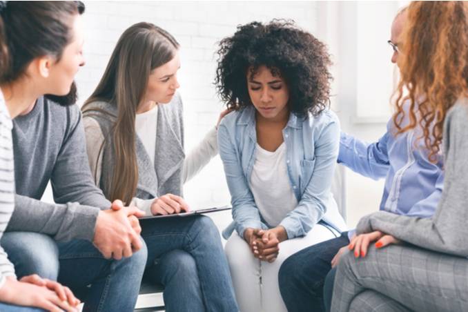 Woman in group therapy setting receiving comfort from other clients