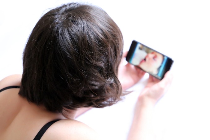 Woman watching porn on mobile phone, thinking of need for porn addiction recovery