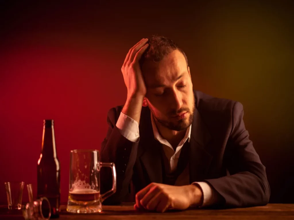 A man contemplates cold turkey detox from alcohol surrounded by drinks at a bar