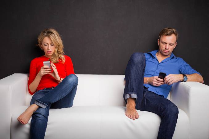 Couple sitting on opposite ends of a couch, each absorbed by their phones and social media