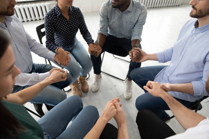 Six people holding hands in group therapy circle, close-up of hands