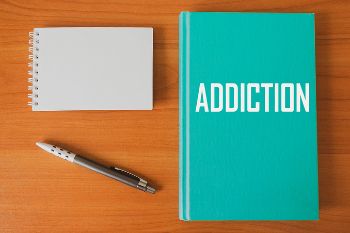 Blank notepad and pen, next to book titled ADDICTION, to indicate readiness to write for Find Addiction Rehabs