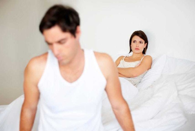 A man at the front of the bed with his wife looking on angrily, to show harm of porn addiction 