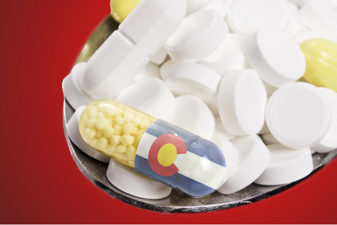 Spoon with various pills, one with logo of Colorado on it, to emphasize both addiction and treatment options in the state
