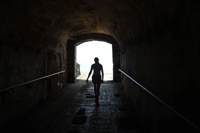 A woman's figure emerges from a tunnel, to show the concept of 5 easy ways to help someone with addiction into the light of recovery