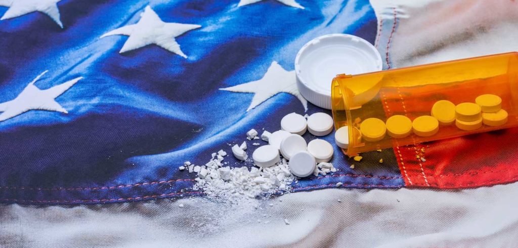 Reducing the Terrible Cost of Addiction, as shown by pills crushed over the American Flag