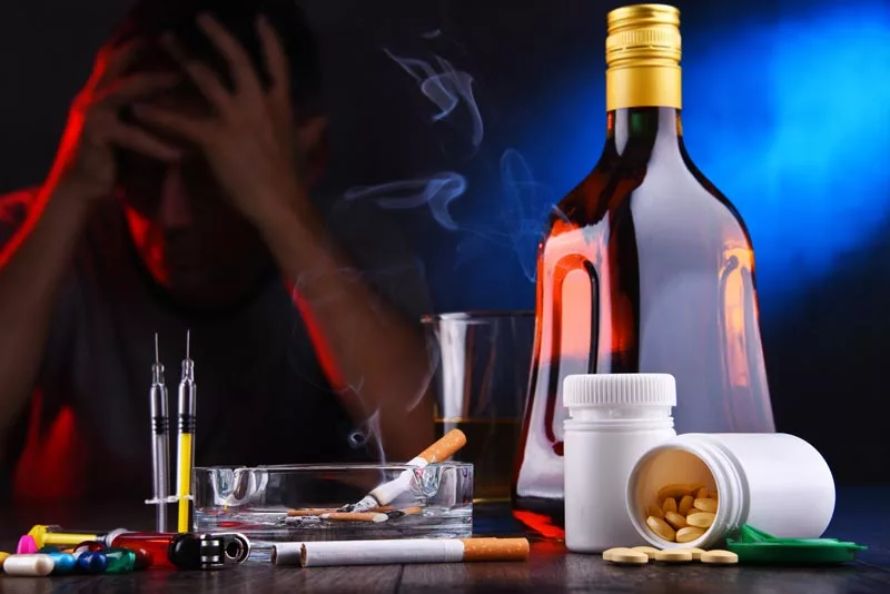 HPPD - Hallucinogenic Persisting Perception Disorder as shown by a man holding his with alcohol and pills nearby