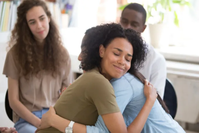 Long term sobriety concept, as shown by women hugging in group therapy