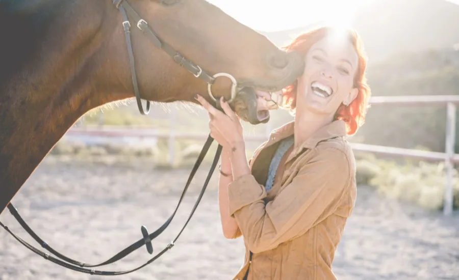 A woman smiles at a horse licking her, to show equine therapy in Texas concept