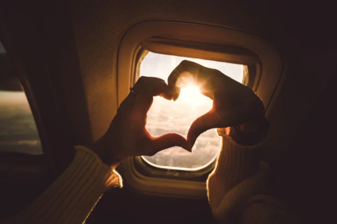 Heart shaped hands in front of airplane window show the promise of travel out of state for GEHA insurance holders