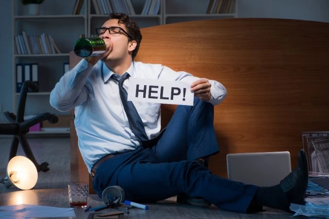 A business man drinking holds up a help sign: to show concept of alcoholic needing rehab